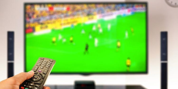 watching soccer at home tv with remote control on hand