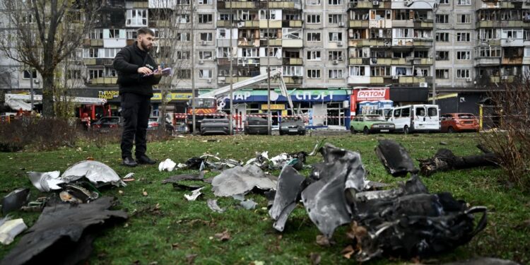 A law enforcement officer inspects debris of an unidentified object in front of a damaged residential building following an air attack in Kyiv on November 29, 2025, amid the Russian invasion in Ukraine. A Russian drone attack targeted the Ukrainian capital in the early hours of November 29, 2025, killing one person and wounding seven, authorities in Kyiv said. (Photo by Genya SAVILOV / AFP)