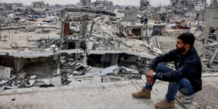 A displaced Palestinian man sits in a damaged building overlooking destruction in the Tel al-Hawa neighborhood, in the southern part of Gaza City, on November 29, 2025. The health ministry in Hamas-run Gaza on November 29 said more than 70,000 people have been killed since the war between Israel and Hamas erupted more than two years ago. The milestone comes as a fragile US-brokered ceasefire largely holds, but with both sides accusing the other of violating the terms of the deal. (Photo by Omar AL-QATTAA / AFP)