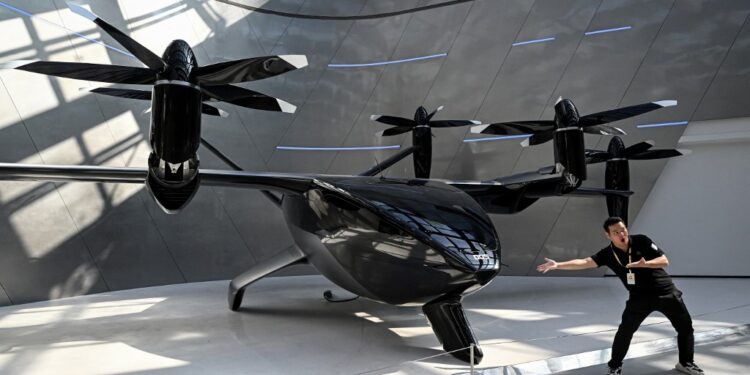 (FILES) A journalist poses next to Xpeng's latest A868 flying car during a showroom tour in Guangzhou, in southern China's Guangdong province on November 5, 2025. Globally, technical and regulatory challenges have prevented the much-hyped flying car sector from getting off the ground. But Chinese companies are building on rapid development of drones and electric vehicles in the world's second largest economy, while harnessing government support for the futuristic inventions. (Photo by Jade GAO / AFP) / To go with AFP story China-economy-technology-automobile-drone, FOCUS by Luna Lin