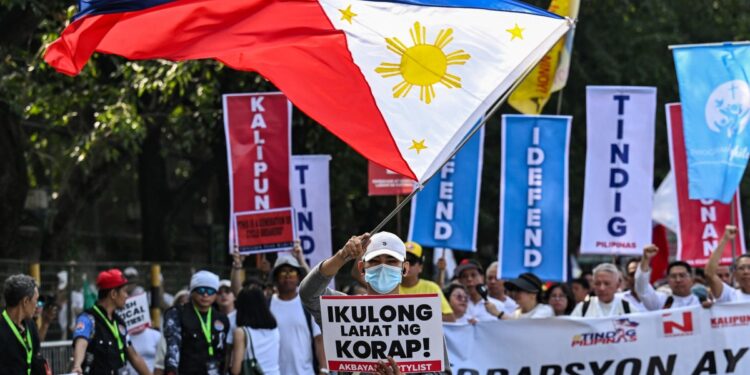 A protester with a Philippine flag marches with a placard that reads "jail all the corrupt" during an anti-corruption rally along Epifanio de los Santos Avenue, or EDSA, in Quezon City, Metro Manila on November 30, 2025. Thousands massed in the Philippine capital on November 30 demanding accountability over a multi-billion-dollar infrastructure scandal that has seen scores of officials, lawmakers and construction firm owners accused of corruption. (Photo by Jam STA ROSA / AFP)