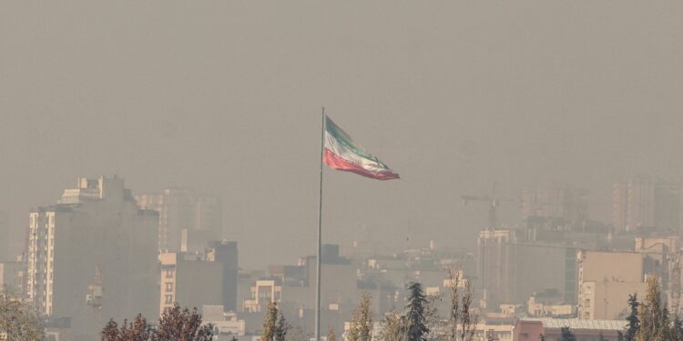 The Iranian flag flutters over the capital blanketed in winter's heavy smog pollution, in Tehran on November 25 2025. (Photo by ATTA KENARE / AFP)