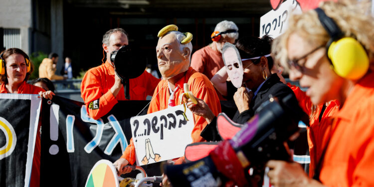 A demonstrator wearing a mask depicting Israeli President Isaac Herzog pretends to feed a banana to another demonstrator wearing a mask depicting Israeli Prime Minister Benjamin Netanyahu during a protest after Netanyahu requested a pardon in his corruption trial, outside a courthouse in Tel Aviv, Israel, December 1, 2025. REUTERS/Amir Cohen