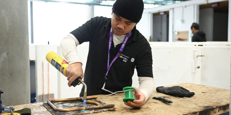 A plumbing student solders a copper pipe during a plumbing class at City of Westminster College, Paddington, in London, Britain, November 20, 2025. REUTERS/Jaimi Joy